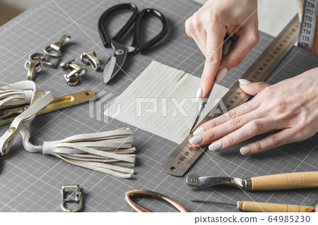 Woman cutting leather fringe for handbag details 64985230