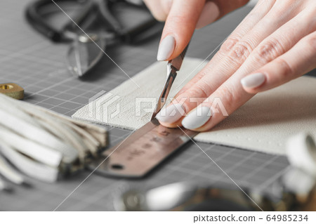 Woman measuring and cutting leather in a workshop 64985234