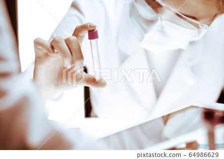 Coronavirus pandemic. Professional female scientist in protective eyeglasses researching tube with reagents in laboratory. Concepts of medicine and virus protection 64986629