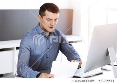 Businessman working with computer in modern sunny office. Headshot of male entrepreneur or company director at workplace. Business concept Businessman working with computer in modern sunny office. Headshot of male entrepreneur or company director at workplace. Business concept 64986654