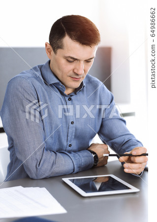 Businessman working with computer in modern sunny office. Headshot of male entrepreneur or company director at workplace. Business concept Businessman working with computer in modern sunny office. Headshot of male entrepreneur or company director at workplace. Business concept 64986662