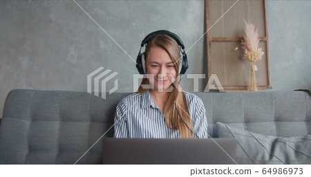 Portrait of happy healthy freelance worker woman using laptop and headphones to work from home on self isolation period. Portrait of happy healthy freelance worker woman using laptop and headphones to work from home on self isolation period. 64986973
