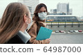 Side view two young Caucasian doctor women wearing face masks, walking on empty city street with clipboards on lockdown. 64987000