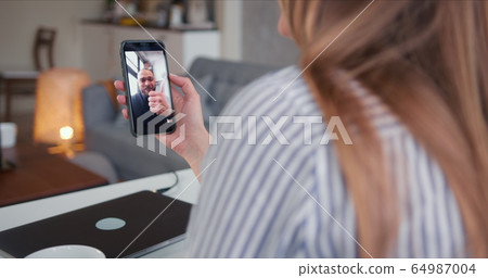 POV close-up young Caucasian woman talking to cheerful male friend on self isolation using smartphone video call online. POV close-up young Caucasian woman talking to cheerful male friend on self isolation using smartphone video call online. 64987004