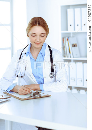 Young woman doctor at work while filling up medication history records in hospital office. Physician controls exam results. Medicine and healthcare concept Young woman doctor at work while filling up medication history records in hospital office. Physician controls exam results. Medicine and healthcare concept 64987282