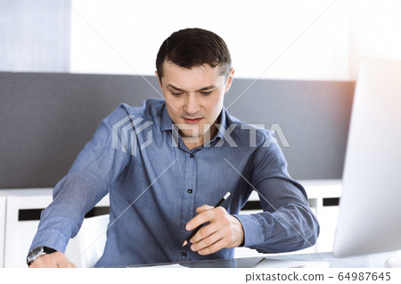 Businessman working with computer in modern sunny office. Headshot of male entrepreneur or company director at workplace. Business concept Businessman working with computer in modern sunny office. Headshot of male entrepreneur or company director at workplace. Business concept 64987645