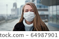 Epidemic quarantine. Portrait of young Caucasian woman wearing mask outdoors, turning head to camera in empty street. 64987901