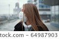 Epidemic quarantine. Portrait of young Caucasian woman wearing mask outdoors, turning head to camera in empty street. 64987903