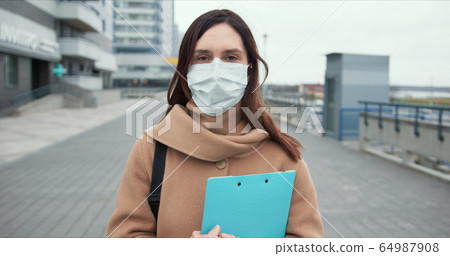 Epidemic control worker. Portrait of Caucasian social care woman in medical face mask in empty street during quarantine. Epidemic control worker. Portrait of Caucasian social care woman in medical face mask in empty street during quarantine. 64987908