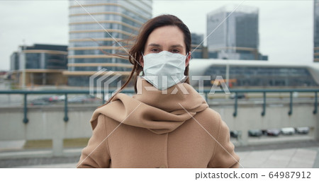 COVID-19 epidemic protection, danger and fear atmosphere. Portrait of beautiful Caucasian woman putting mask on outside. COVID-19 epidemic protection, danger and fear atmosphere. Portrait of beautiful Caucasian woman putting mask on outside. 64987912
