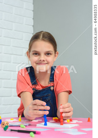 Girl plays board games, sits at a table at home Girl plays board games, sits at a table at home 64988335