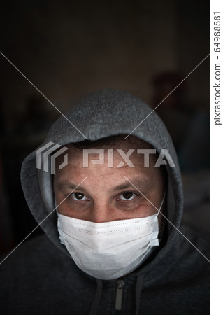 Young adult male with a gray hood in a medical mask. Restless serious look straight. Dark gray 64988881