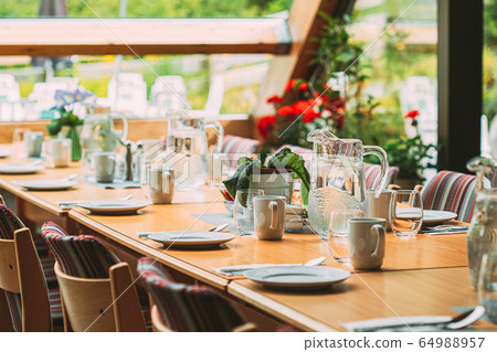 Cozy Interior Of Summer Cafe. Jug Of Water On Table And Cutlery Laid Out 64988957