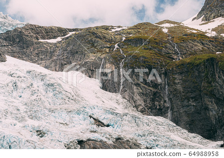 Jostedalsbreen National Park, Norway. Close Up View Of Melting Ice And Snow, Small Waterfall On Boyabreen Glacier In Spring Sunny Day. Famous Norwegian Landmark And Popular Destination. Close Up 64988958