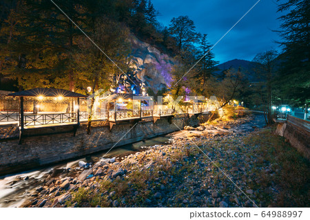 Borjomi, Georgia. Night View Of Borjomula Mountain River Passing Through City, Park And Street Gazebo. Landscape Of Rocky River At Evening Night Illumination. Borjomi, Georgia. Night View Of Borjomula Mountain River Passing Through City, Park And Street Gazebo. Landscape Of Rocky River At Evening Night Illumination. 64988997