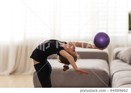 Little girl gymnast performs various gymnastic and fitness exercises at home. The concept of childhood and sport, a healthy lifestyle 64989662