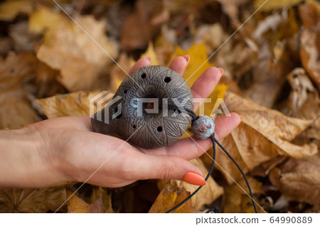Female hand with orange manicure holds ceramic ocarina in the forest during autumn. Relaxing tranquil scene, traditional music concepts Female hand with orange manicure holds ceramic ocarina in the forest during autumn. Relaxing tranquil scene, traditional music concepts 64990889