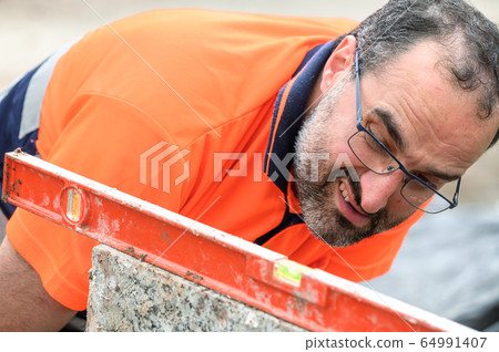 Construction worker checking the bubble level while working at construction site. Building Construction worker checking the bubble level while working at construction site. Building 64991407