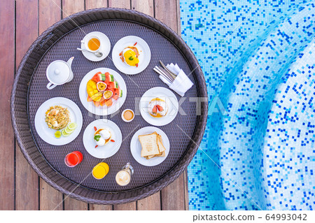 Flotaing breakfast tray around outdoor swimming pool with bread fruit egg coffee and juice Flotaing breakfast tray around outdoor swimming pool with bread fruit egg coffee and juice 64993042