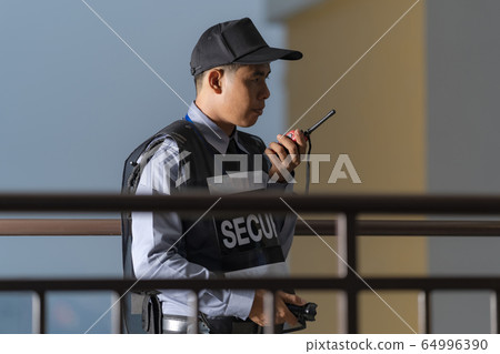 Security man standing outdoors using portable 64996390