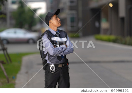 Security man standing outdoors near big building 64996391