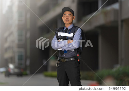 Security man standing outdoors near big building 64996392