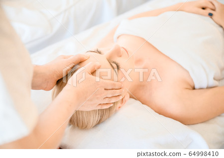 Beautiful woman receiving head and facial massage in spa salon 64998410