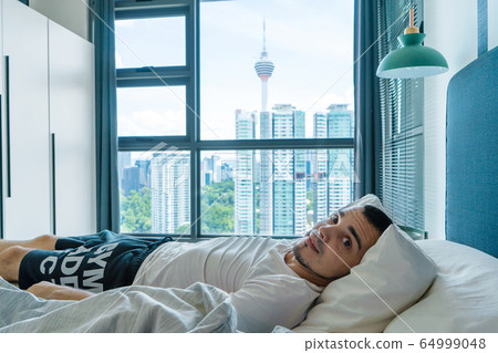 The guy is lying on the bed near the window with The guy is lying on the bed near the window with 64999048