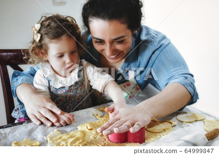 Mother and daughter baking cookies in the kitchen - cutting pastry dough with plastic shape cutters Mother and daughter baking cookies in the kitchen - cutting pastry dough with plastic shape cutters 64999847