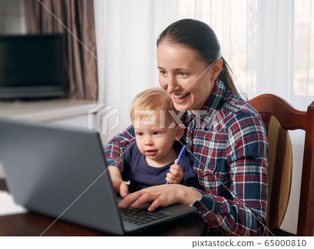 Stay at home mom working remotely on laptop while taking care of her baby. 65000810