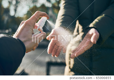 Male's hand spraying sanitizer on woman's hands outdoors to disinfect hands 65000855