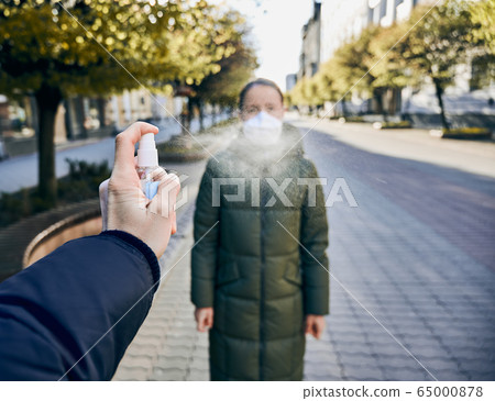 Male's hand using sanitizer to disinfect hands, woman in mask on empty street during quarantine time 65000878