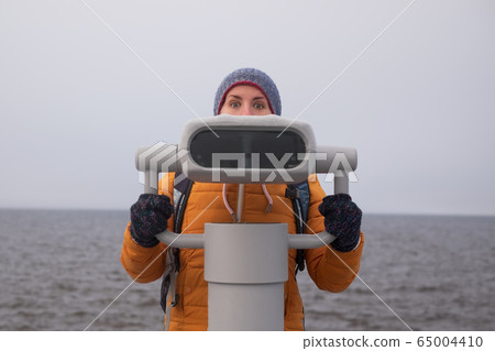 Young woman looking through a coin operated 65004410