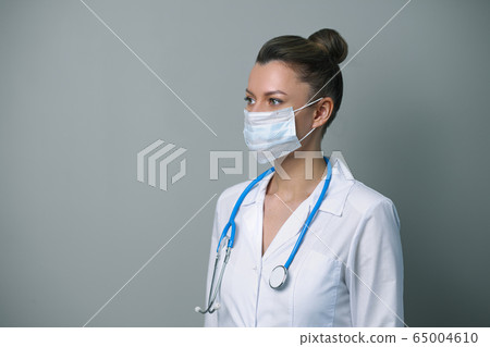 A female doctor in a white robe and mask with a stethoscope. A female doctor in a white robe and mask with a stethoscope. 65004610