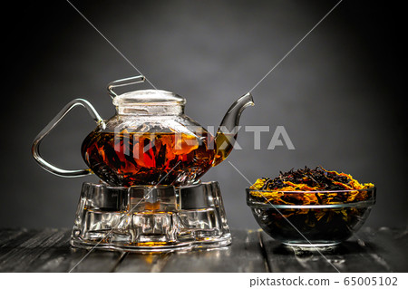 Horizontal photo of the tea set on a black background. Glass transparent teapot and cup. Black leaf tea. Horizontal photo of the tea set on a black background. Glass transparent teapot and cup. Black leaf tea. 65005102
