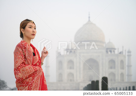Asian woman wearing red saree indian traditional dress against Taj Mahal 65005133