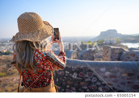 Rear view of young woman traveler capturing view of Jaswant Thada and Mehrangarh Fort in Jodhpur 65005154