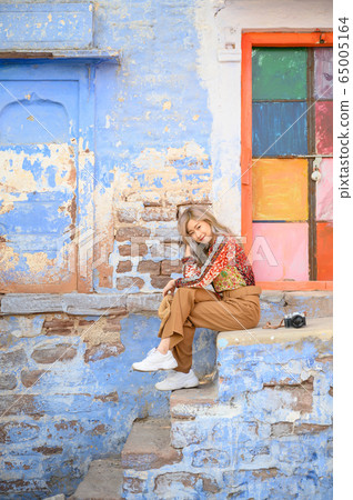 Portrait of young woman in front colorful building wall in Jodphur blue city in India 65005164