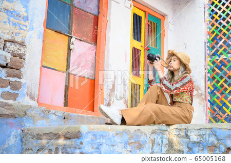 Portrait of young woman in front colorful building wall in Jodphur blue city in India 65005168