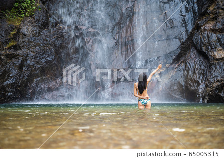 Young slim woman in Bikini enjoys waterfall Young slim woman in Bikini enjoys waterfall 65005315