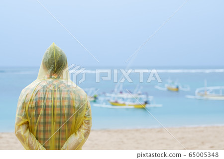 Man in a yellow raincoat on tropical seashore 65005348