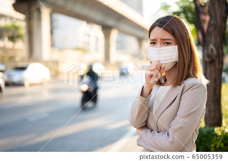 Young business woman wearing surgical mask and coughing while walking in public Young business woman wearing surgical mask and coughing while walking in public 65005359