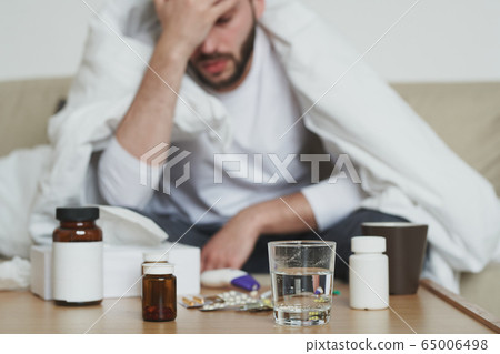 Group of bottles with pills and glass of water on table and sick young man Group of bottles with pills and glass of water on table and sick young man 65006498