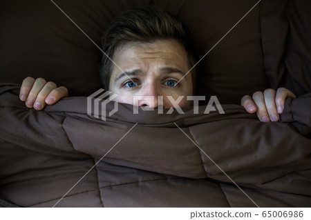 Caucasian young man hiding in bed under the Caucasian young man hiding in bed under the 65006986