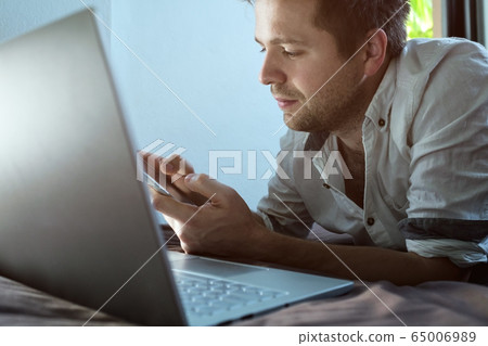 Caucasian young man lying on bed at his laptop. 65006989