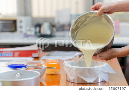 Woman pouring dough for a cake into an aluminum mold padded with parchment paper. Woman pouring dough for a cake into an aluminum mold padded with parchment paper. 65007197