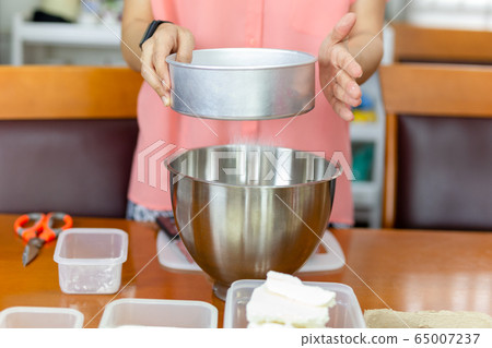 Woman sifts flour in a metal bowl preparing to bake a cake. 65007237