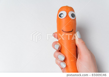 Hand holding carrot with fun Googly eyes and smile 65009146