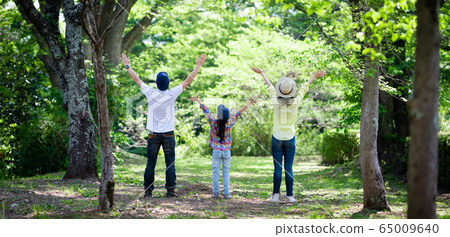 Family of three spreading both hands in the forest 65009640