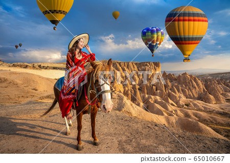 Tourists enjoy ride horses and looking to balloons in Cappadocia, Turkey 65010667